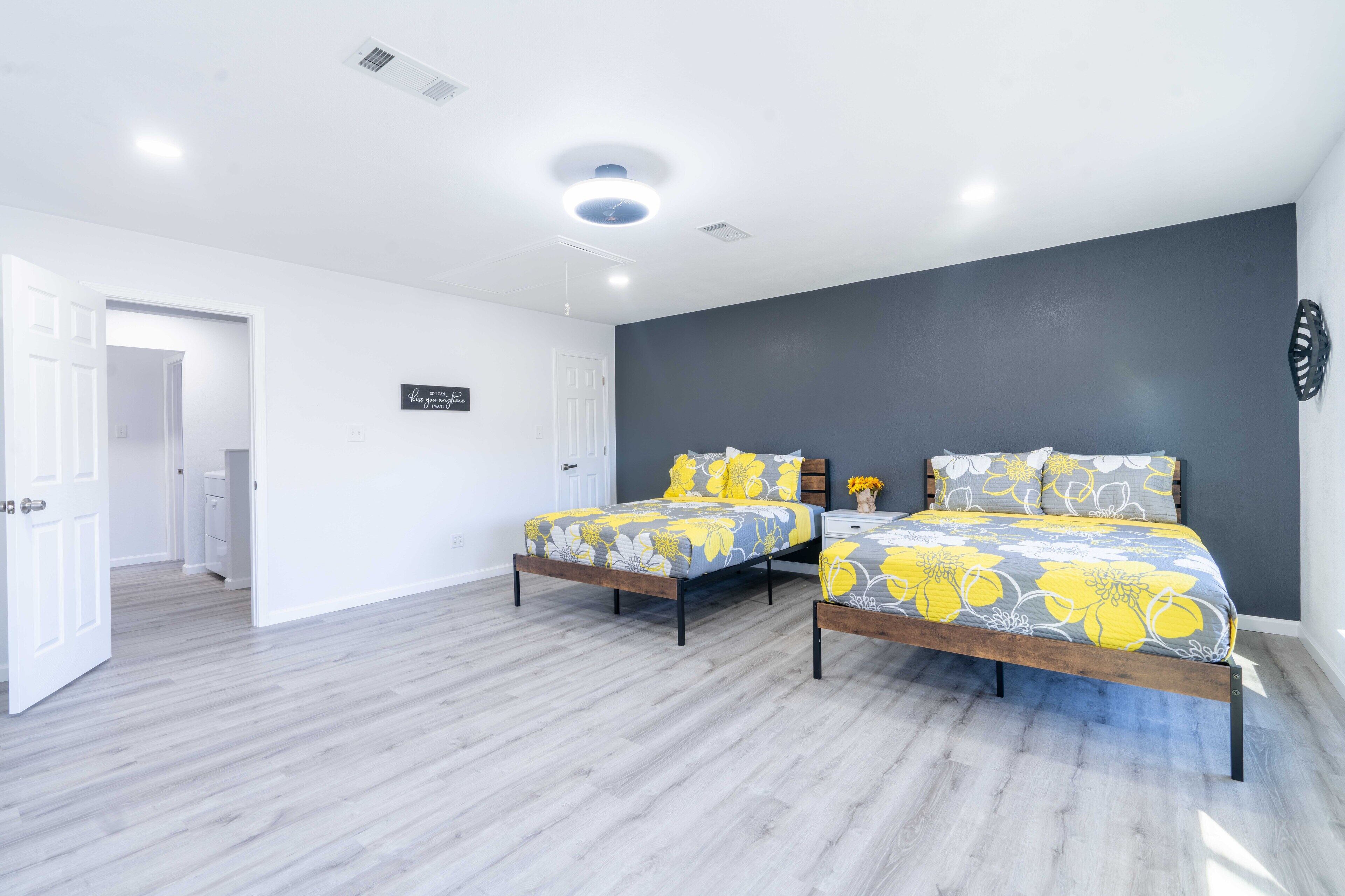 A bedroom with two beds, a dark accent wall, and a white door leading to another room.