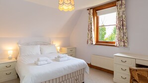 Une chambre à coucher comprenant un lit, des tables de chevet, un bureau, une chaise, un radiateur et une fenêtre avec des rideaux.