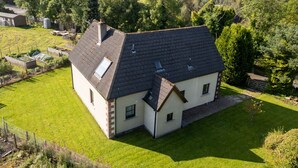 Une grande maison de plain-pied, dotée d’un toit en pente, entourée d’une pelouse bien entretenue et bordée, à l’arrière, d’une forêt dense.