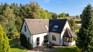 Une maison à deux étages avec un toit en pente, une terrasse en pierre et une petite plateforme en bois.