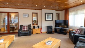 Ein gemütliches Wohnzimmer mit Holzbalkendecke, einem Flachbildfernseher, Ledersofas und einem Couchtisch aus Holz.