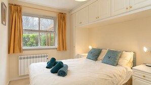 Ein Schlafzimmer mit einem Bett, einem Nachttisch, einer Lampe, einem Fenster mit Vorhängen und einer Heizung.