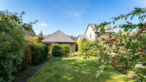 Ein gepflegter Garten mit Rasen, einer Holz-Pergola und reifen Bäumen.