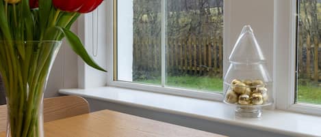 A clear view of a window with a wooden fence outside, a vase with tulips on a table, and a book titled "The Enemy" by Charlie Higson.