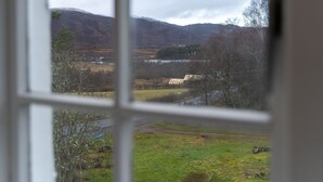 Vista a través de una ventana de un paisaje rural con montañas, un campo y un edificio pequeño.