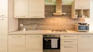 A modern kitchen with light wood cabinets, a stainless steel sink, a gas stove, a microwave, and a built-in oven. - Blue Diamond by Interhome (Bellano)