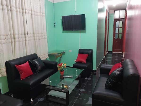 A modern living room with black leather sofas, a glass coffee table, and a flat-screen TV mounted on the wall. - Depa - 204 (Moyobamba)