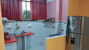 A kitchen with a red countertop, a stainless steel refrigerator, and a window with red curtains. - Depa - 204 (Moyobamba)