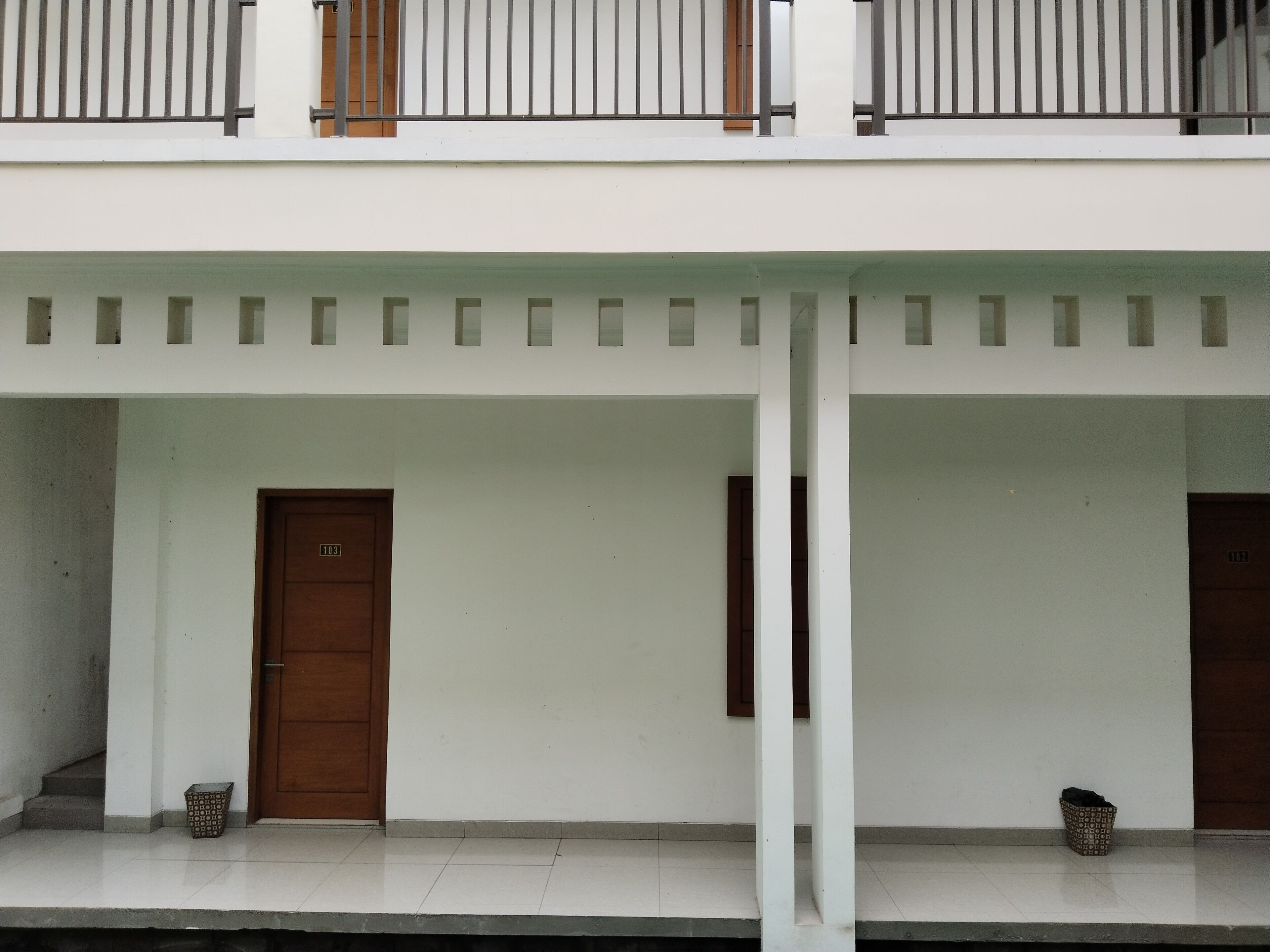 A building with a white exterior, two wooden doors, and a balcony with metal railings.
