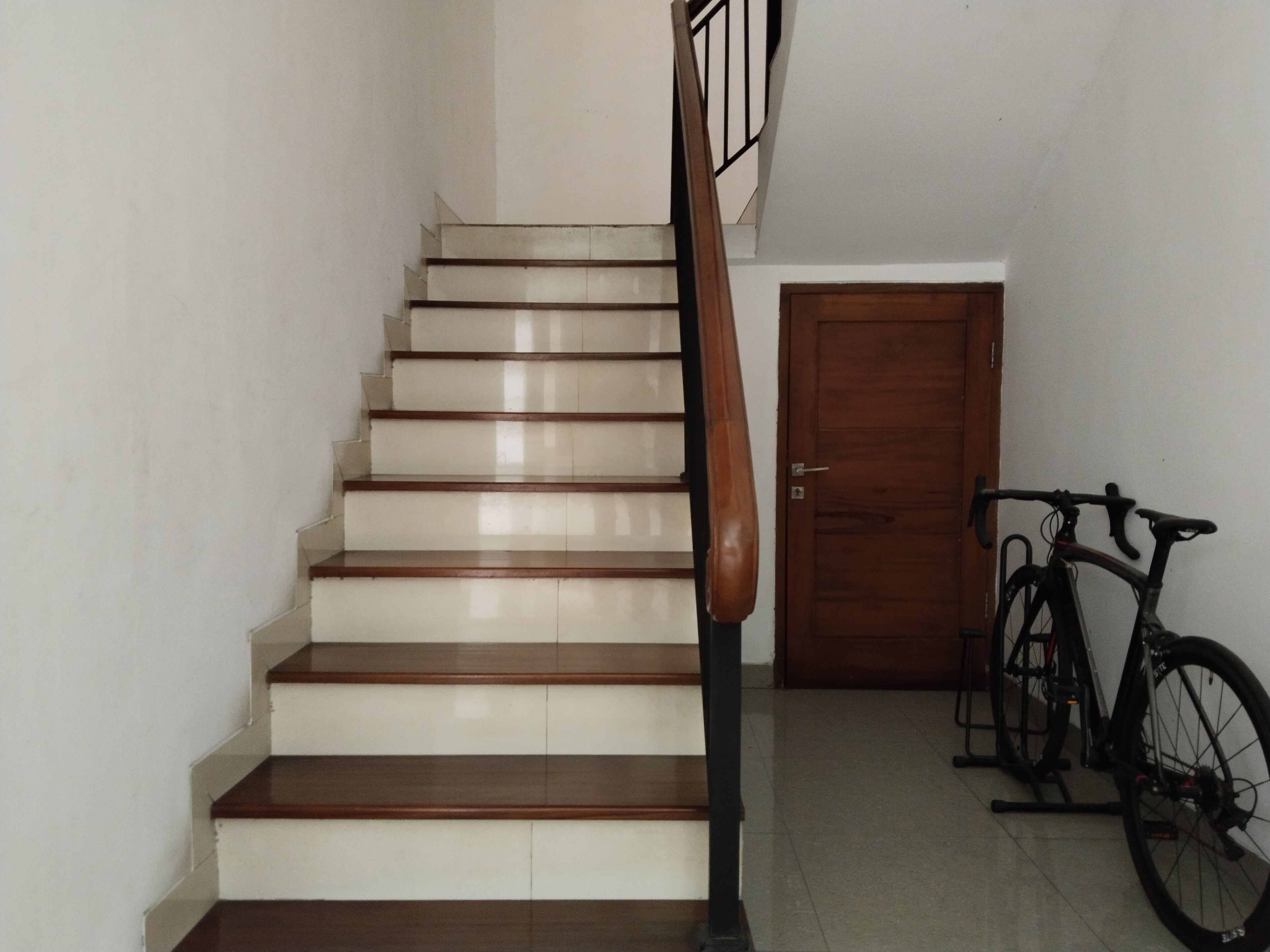 Una escalera con escalones de madera y barandilla, que conduce a una puerta de madera cerrada. Una bicicleta está estacionada contra la pared a la derecha.