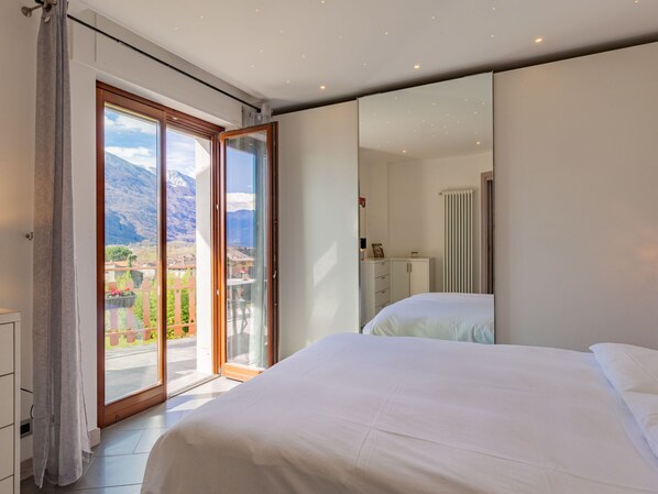 A bedroom with a large bed, a sliding glass door leading to a balcony with a mountain view, and a white wardrobe.