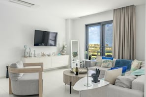 A modern living room with a flat-screen TV, a sofa, a coffee table, and a dining area.