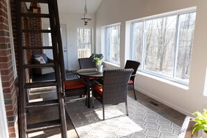 A sunlit patio with a round table, wicker chairs, and a potted plant. - Sunset Cottage:  Spacious Vacation Home with Game Room (Meadville)