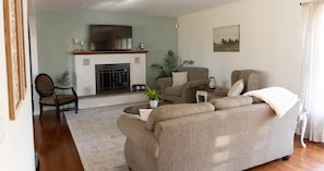 A living room with a fireplace, a sofa, a chair, and a television. - Sunset Cottage:  Spacious Vacation Home with Game Room (Meadville)