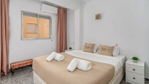 Et pænt hotelværelse med seng, to sengeborde, en lille plante og et vindue med gardiner.