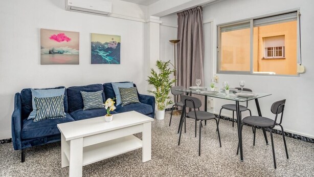 En moderne stue med en blå sofa, et hvidt sofabord og et spiseområde med et glasbord og stole.