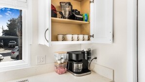 Une cuisine équipée d’une machine à café, de tasses et d’un mixeur sur le plan de travail.