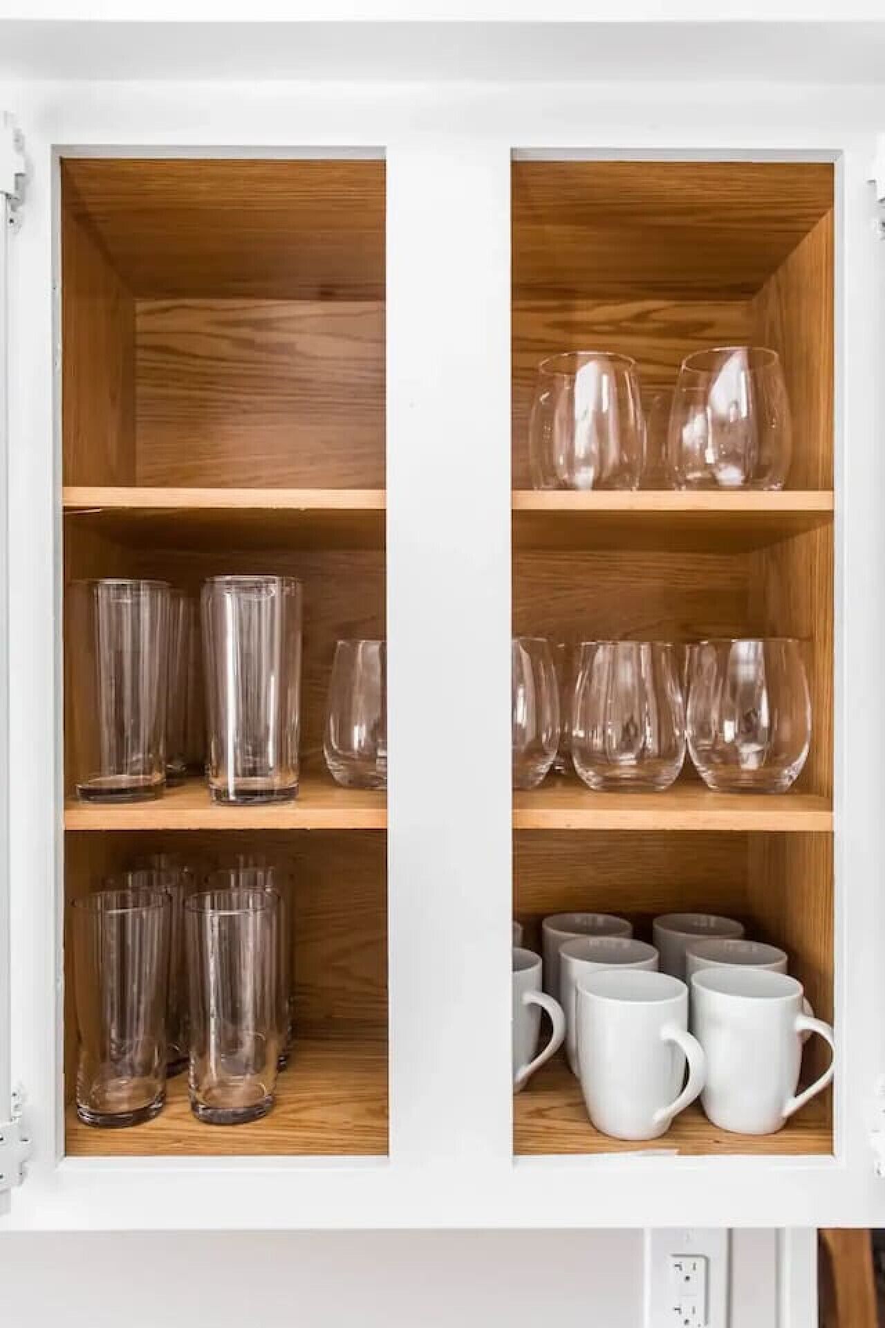Een kast met meerdere planken, gevuld met glazen en witte mokken.