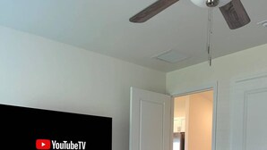 Une chambre dotée d’un téléviseur à écran plat, d’un ventilateur de plafond et d’un lit recouvert d’une couverture à motifs.