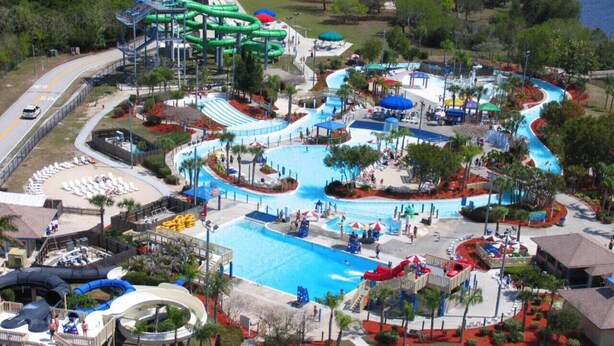 Vue aérienne d’un parc aquatique avec de nombreux toboggans, des piscines et un grand espace central avec une grande piscine.
