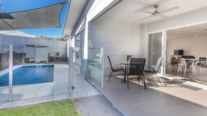 Een modern terras buiten met een zwembad, glazen deuren en een eethoek met stoelen en een tafel.