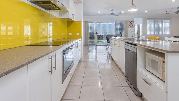 Een moderne keuken met een gele spatwand, witte kasten en roestvrijstalen apparatuur.