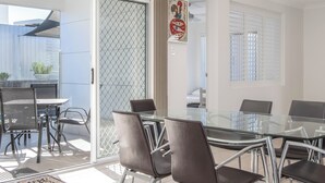Een moderne eetruimte met glazen tafels en stoelen, een schuifdeur van glas naar een balkon en een decoratief wandobject.