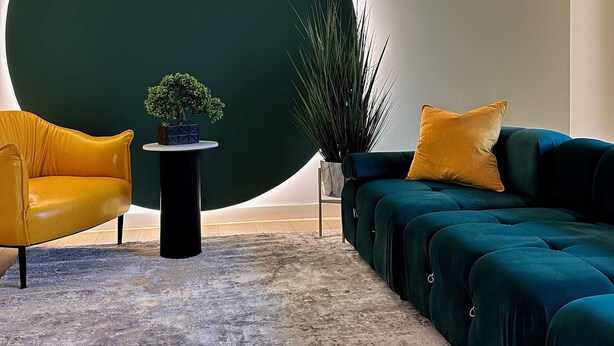 A modern living room with a large circular wall feature, a yellow armchair, a dark green sofa, and a small table with a plant. - Private Parking•Walk Everywhere•Style•King bed (Pittsburgh)