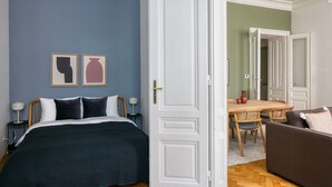 Ein Schlafzimmer mit einem Bett, Nachttischen und einer Tür zu einem Essbereich mit Tisch und Stühlen.