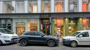 Straßenansicht mit drei geparkten Autos vor einer Reihe von Geschäften, darunter ein Juweliergeschäft namens 'Saboteur'.