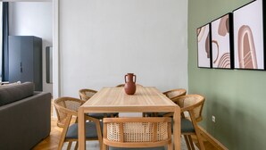 Ein Essbereich mit einem Holztisch, sechs Korbstühlen, einer grauen Couch und einem grauen Schrank im Hintergrund.
