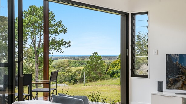 A modern living room with a large sliding glass door leading to a scenic outdoor view. - Take it easy at this unique and tranquil getaway. (Tintenbar)