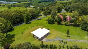 An aerial view of a rural property with a large building, green fields, and a road. - Take it easy at this unique and tranquil getaway. (Tintenbar)
