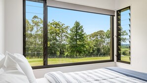 A bedroom with a large window, a bed with striped bedding, and a view of a green landscape. - Take it easy at this unique and tranquil getaway. (Tintenbar)