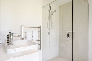 Un baño moderno con lavamanos blanco, cabina de ducha de vidrio y un perchero para toallas.