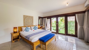 A spacious bedroom with a large bed, wooden headboard, and a view through a sliding glass door to a garden. - Ubud Shanti Rice Field House By Supala (Ubud)