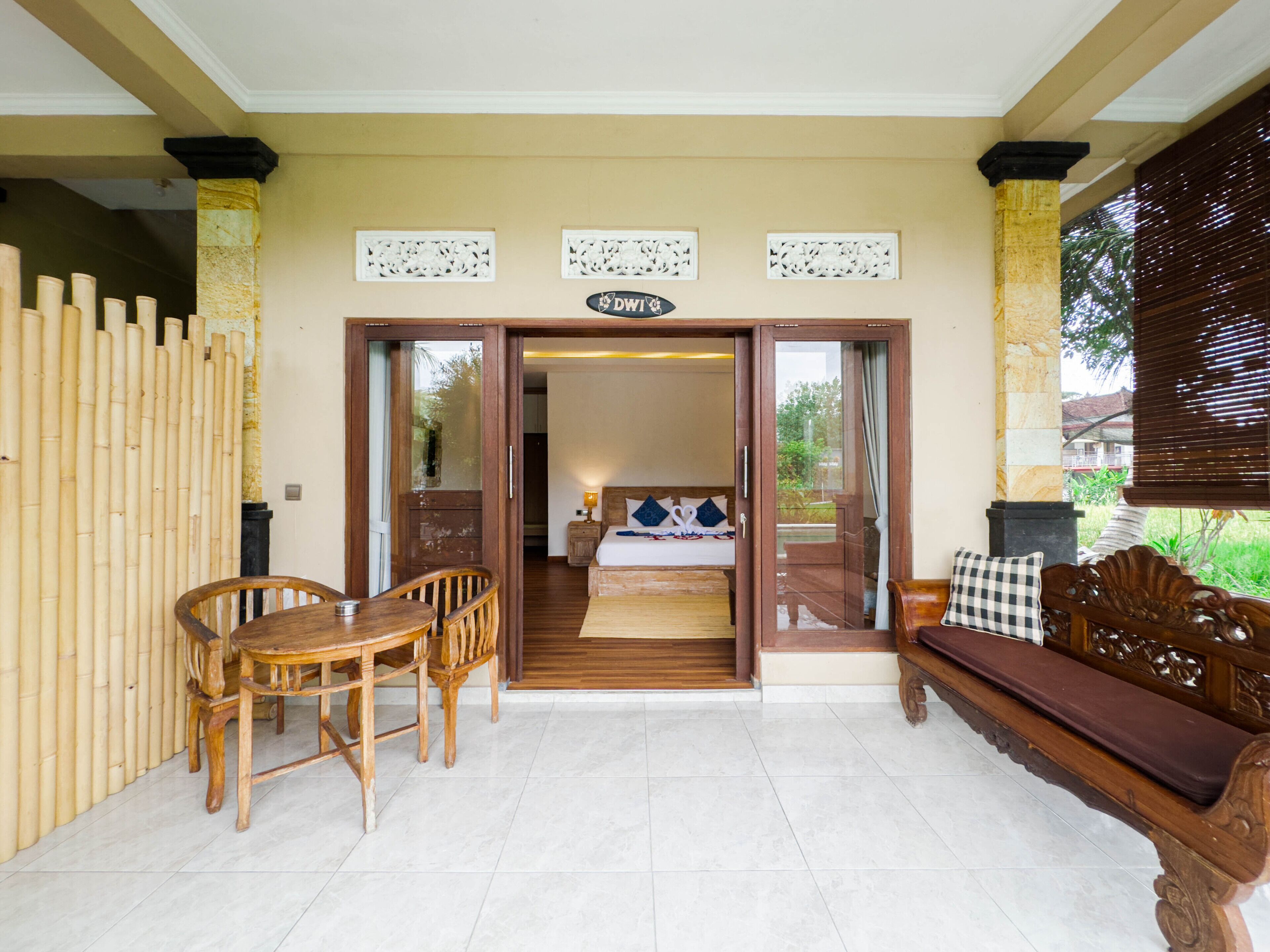A room with a bed, a wooden bench, a table with chairs, and a sign above the door.