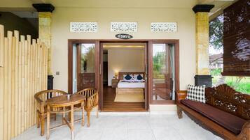 A room with a bed, a wooden bench, a table with chairs, and a sign above the door.
