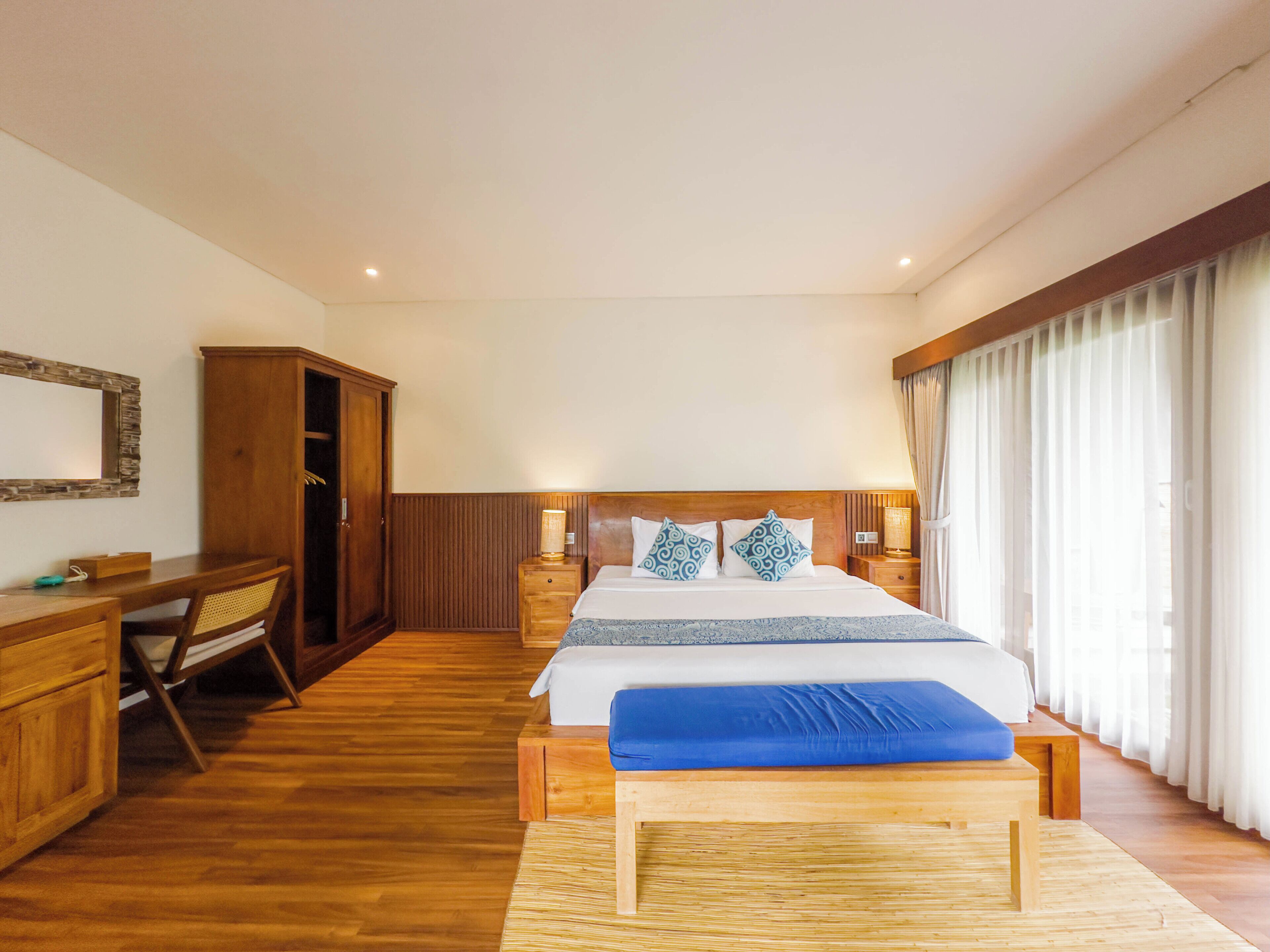 A hotel room with a wooden bed, bedside tables, a desk, and a wardrobe.