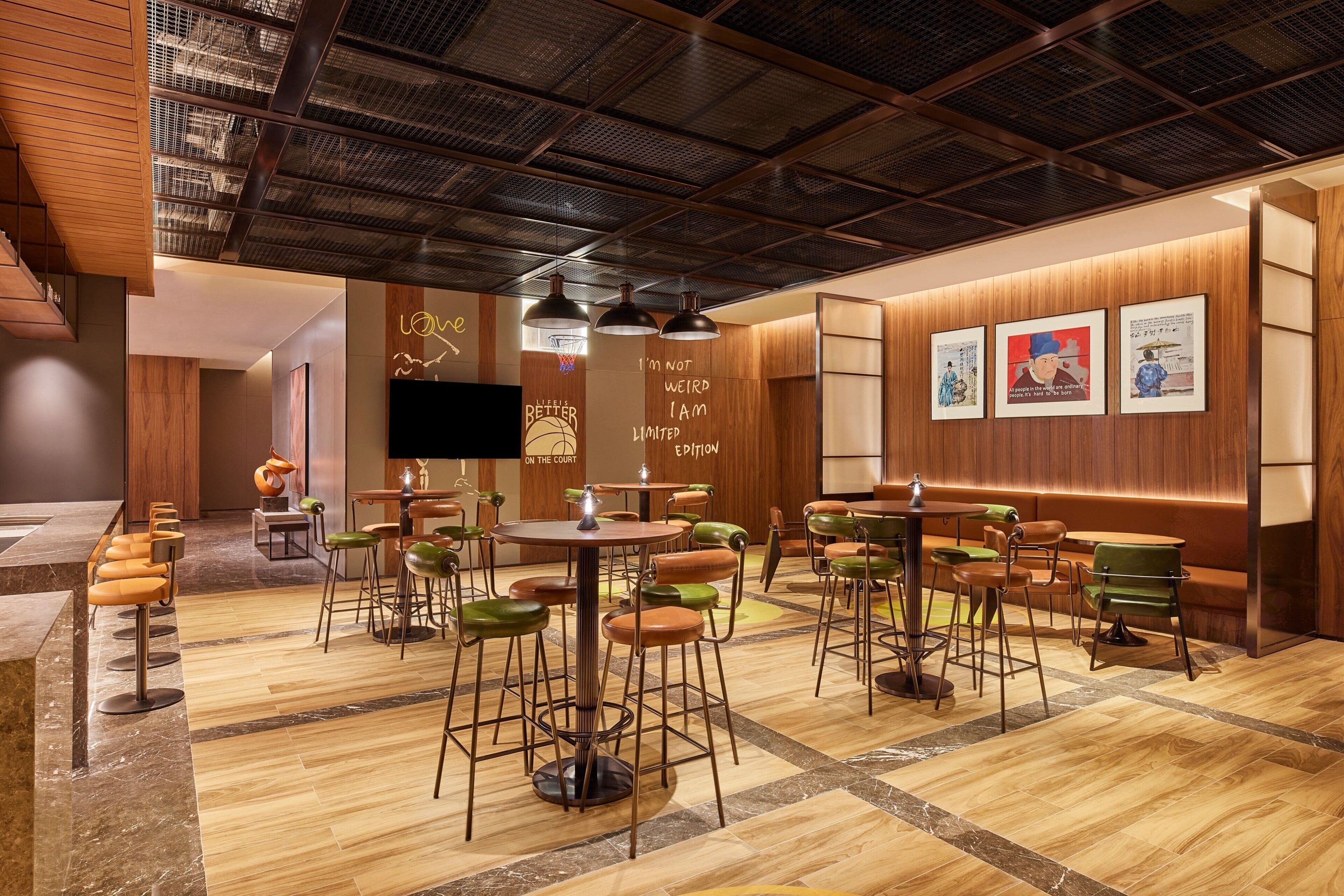 A modern restaurant with wooden walls, a high ceiling, and a mix of green and brown bar stools.