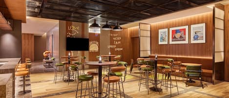 A modern restaurant with wooden walls, a high ceiling, and a mix of green and brown bar stools.