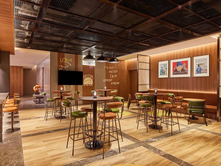 A modern restaurant with wooden walls, a high ceiling, and a mix of green and brown bar stools.