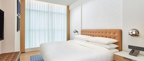 A hotel room with a large bed, a wooden headboard, a bedside table with a phone, and a window with sheer curtains.