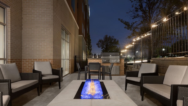 Une terrasse extérieure dotée d’un foyer rectangulaire, de meubles en osier et d’un barbecue.