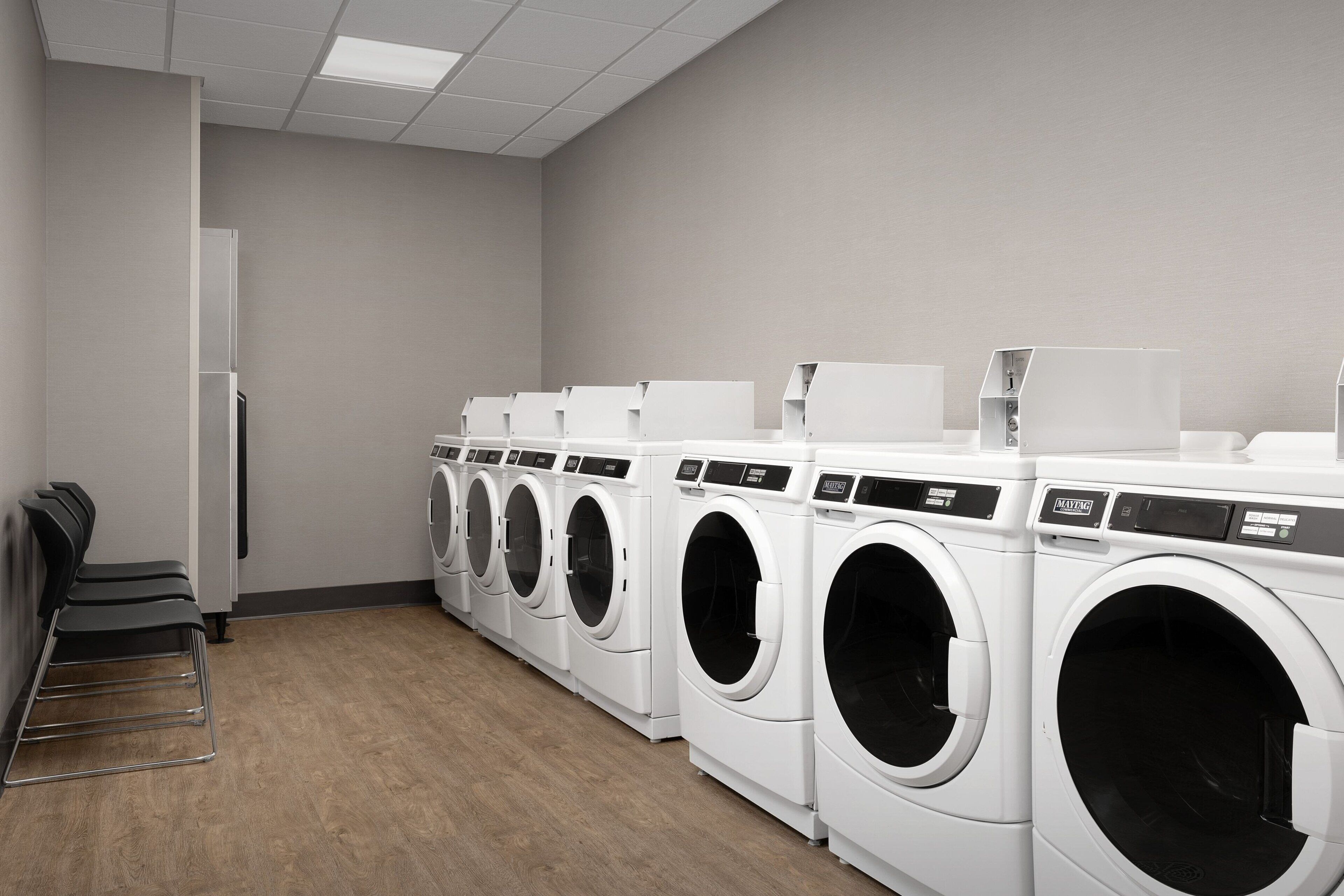 A laundry facility with multiple washing machines and dryers lined up against a wall.