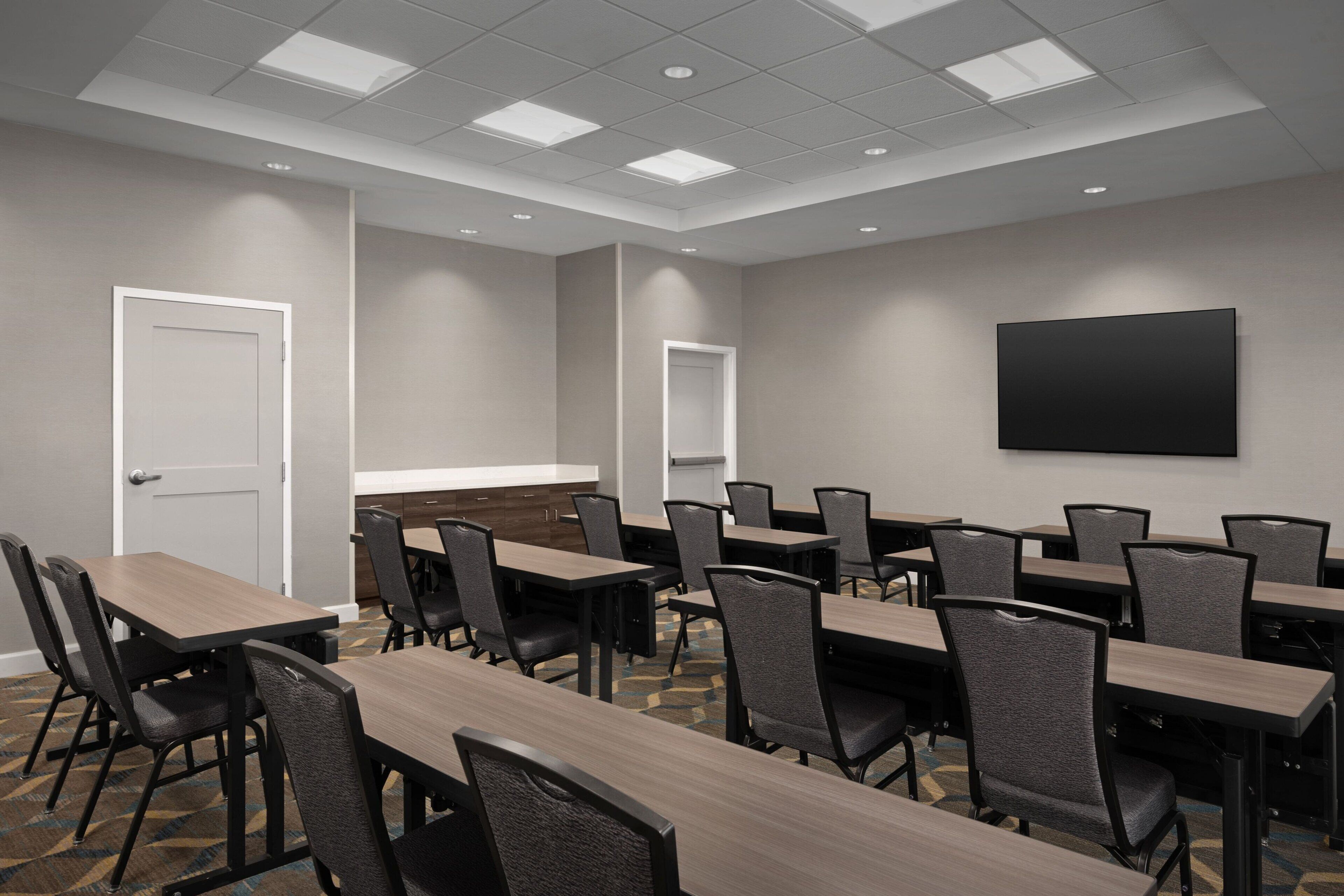 A conference room with multiple tables and chairs, a whiteboard, and a large flat-screen TV on the wall.