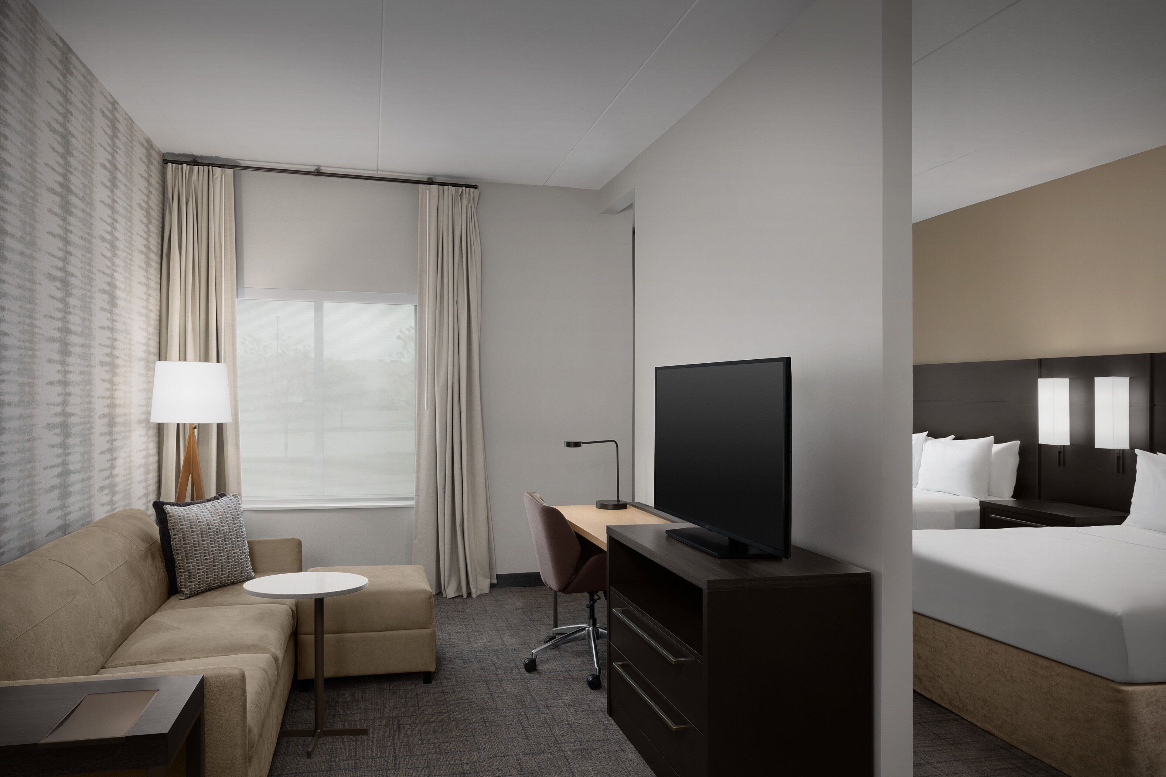 Ein Hotelzimmer mit Bett, Schreibtisch, Fernseher, einer Couch, einem Sessel und einem Fenster mit Vorhängen.