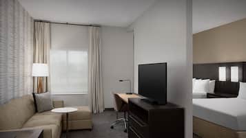 Ein Hotelzimmer mit Bett, Schreibtisch, Fernseher, einer Couch, einem Sessel und einem Fenster mit Vorhängen.