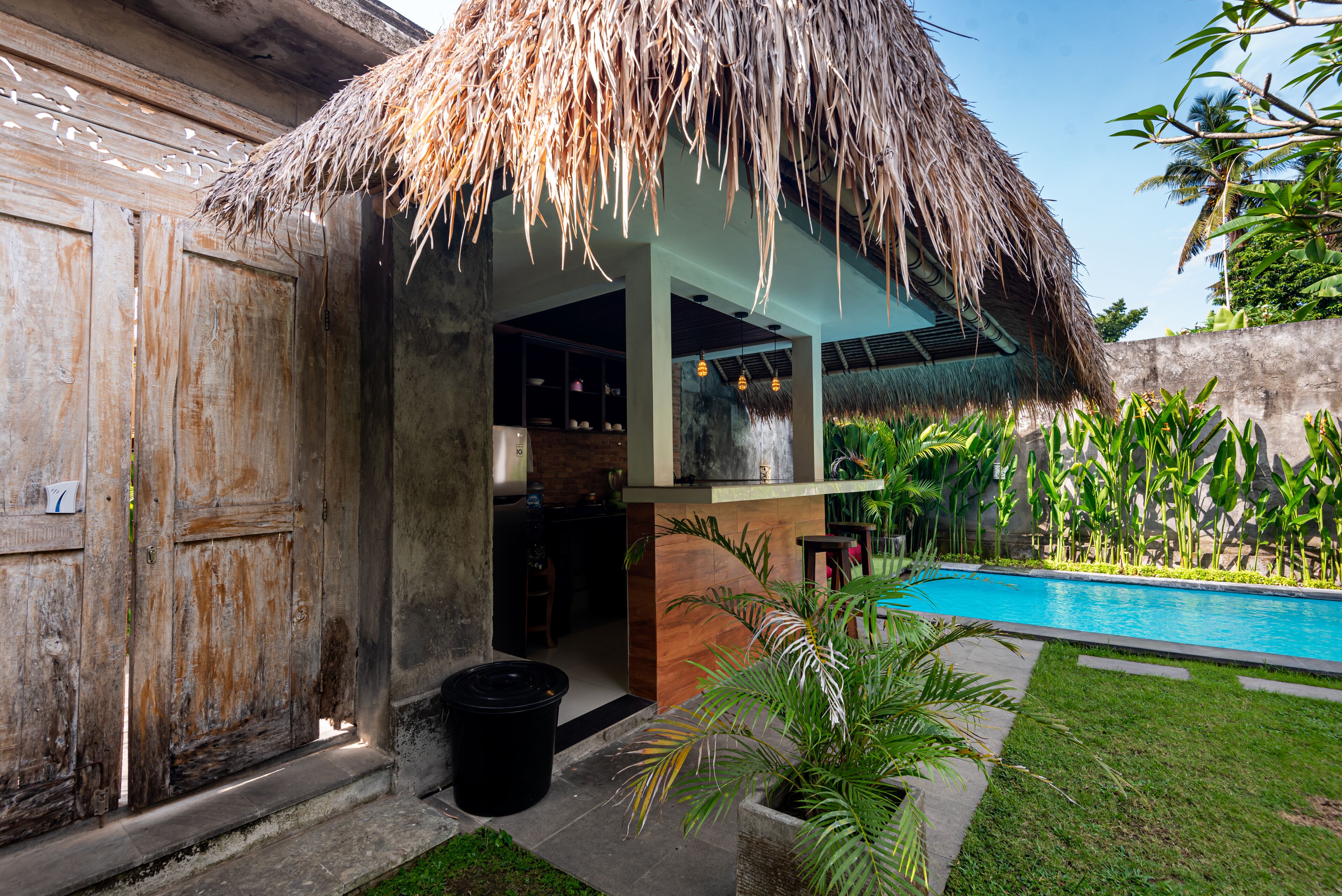 A thatched-roof structure with a pool and lush greenery.