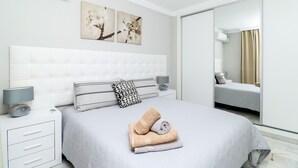 Ein modernes Schlafzimmer mit einem großen Bett, einem Nachttisch mit Lampe und einem Spiegel an der Wand.